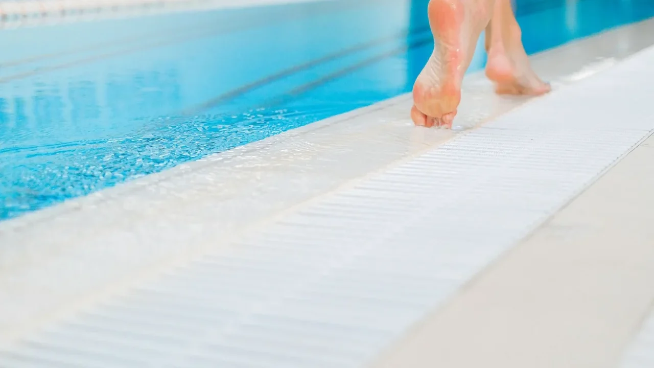 Picioare goale pe marginea uda a unei piscine, pe placi antiderapante